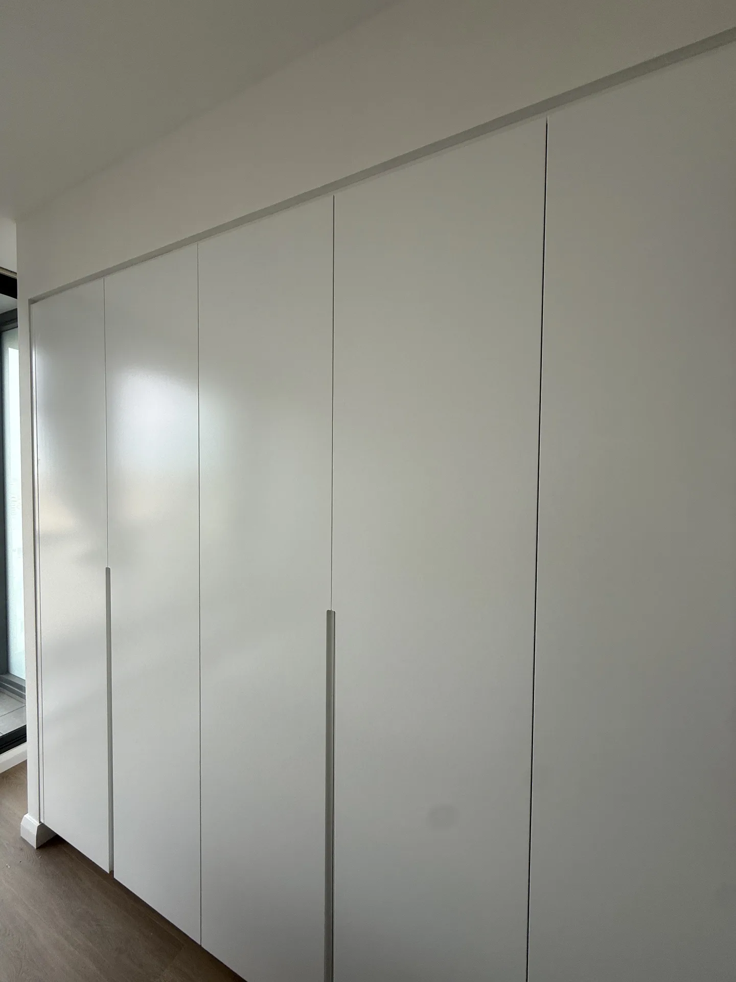 Long wall of floor-to-ceiling white wardrobe doors closed tight to the ceiling line