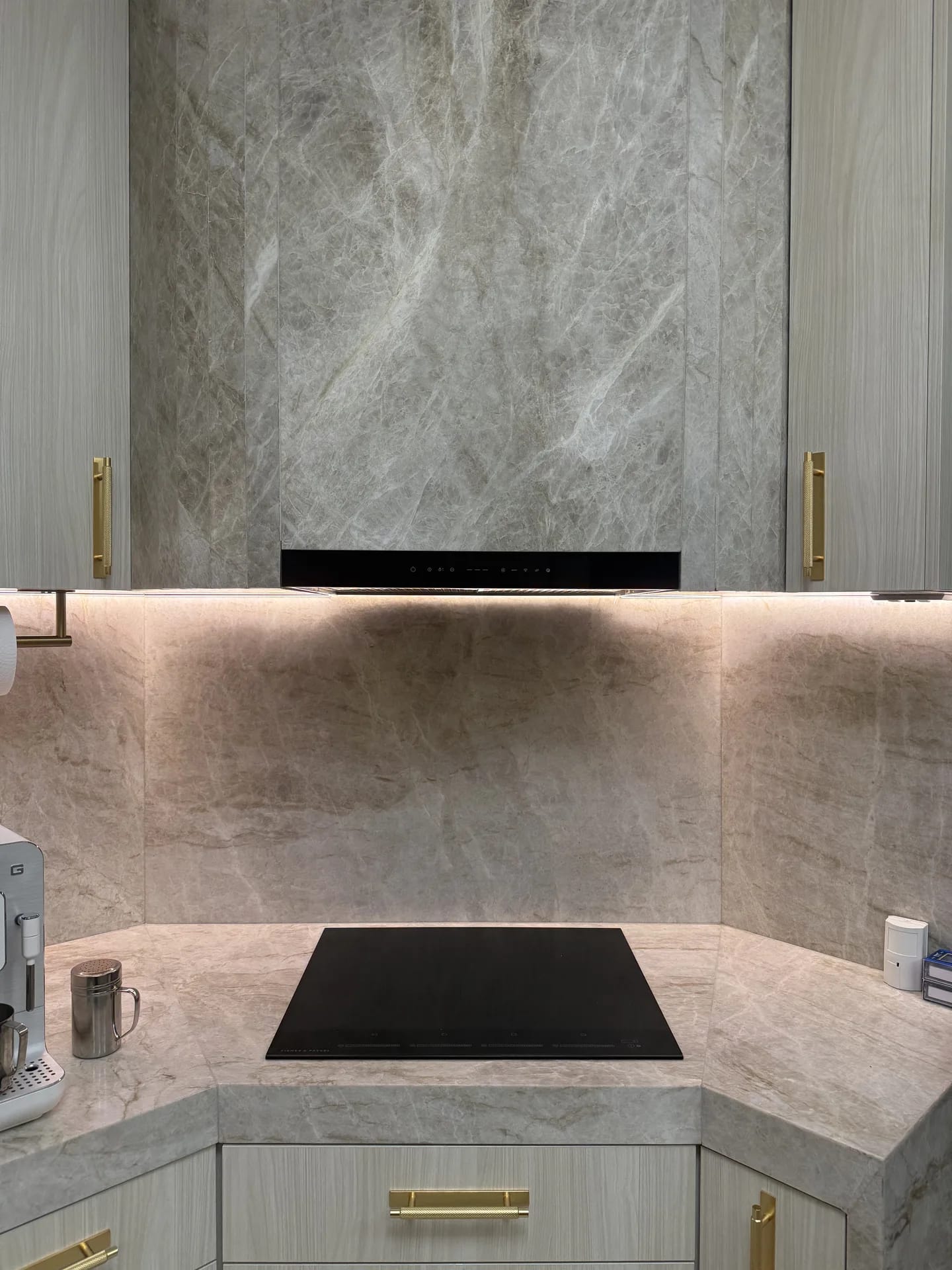 Induction cooktop below a full-height stone splashback and stone-clad rangehood surround