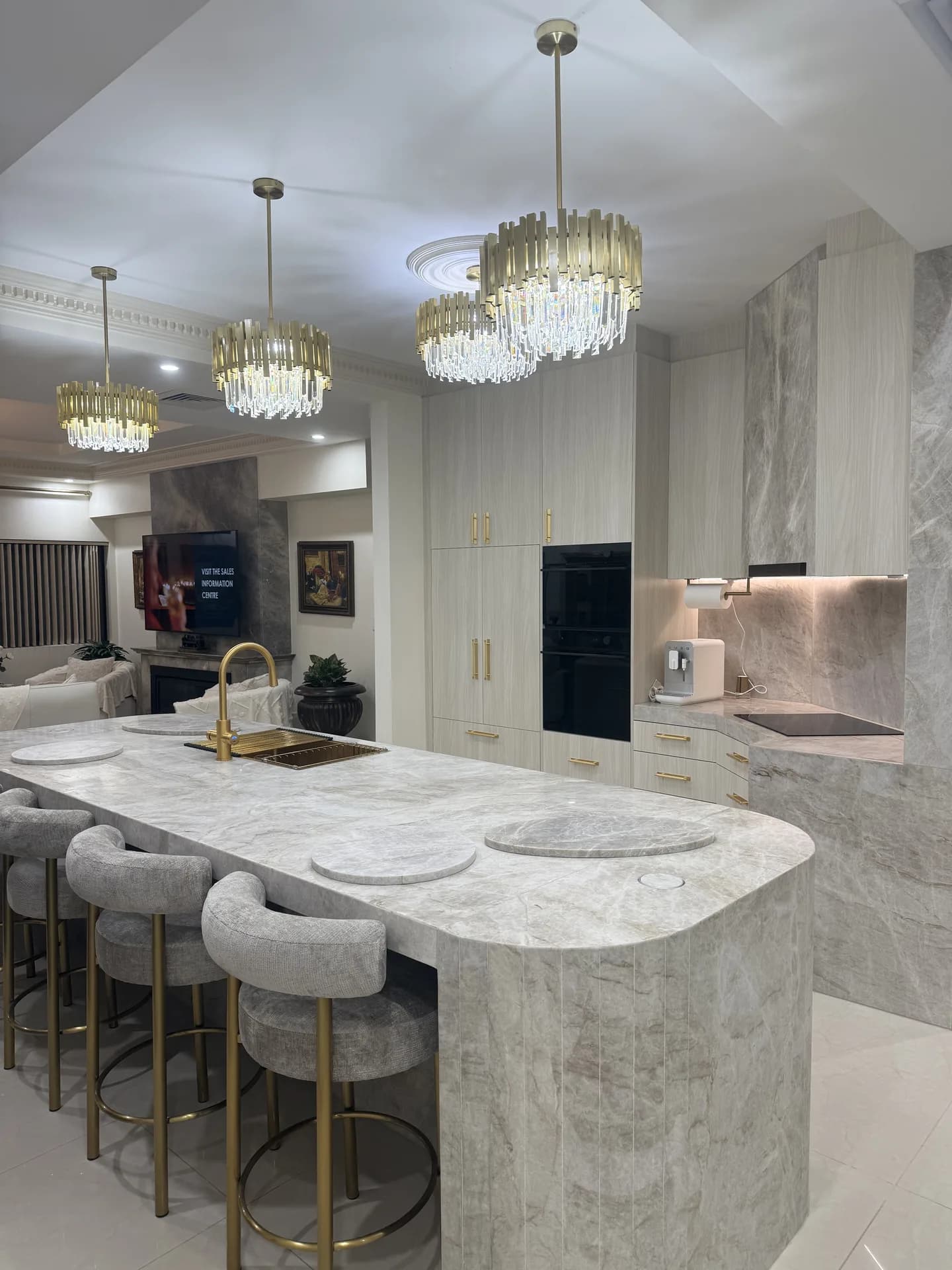 Curved natural stone kitchen island with brass tapware, pale joinery and a stone rangehood beyond