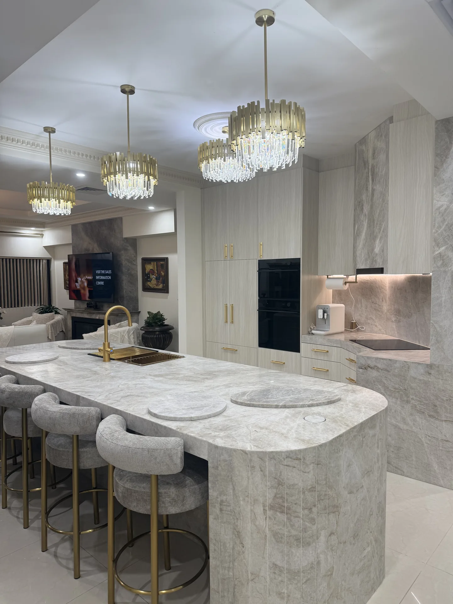 Kitchen island with brass tap, tall pale joinery, black ovens and stone rangehood beyond
