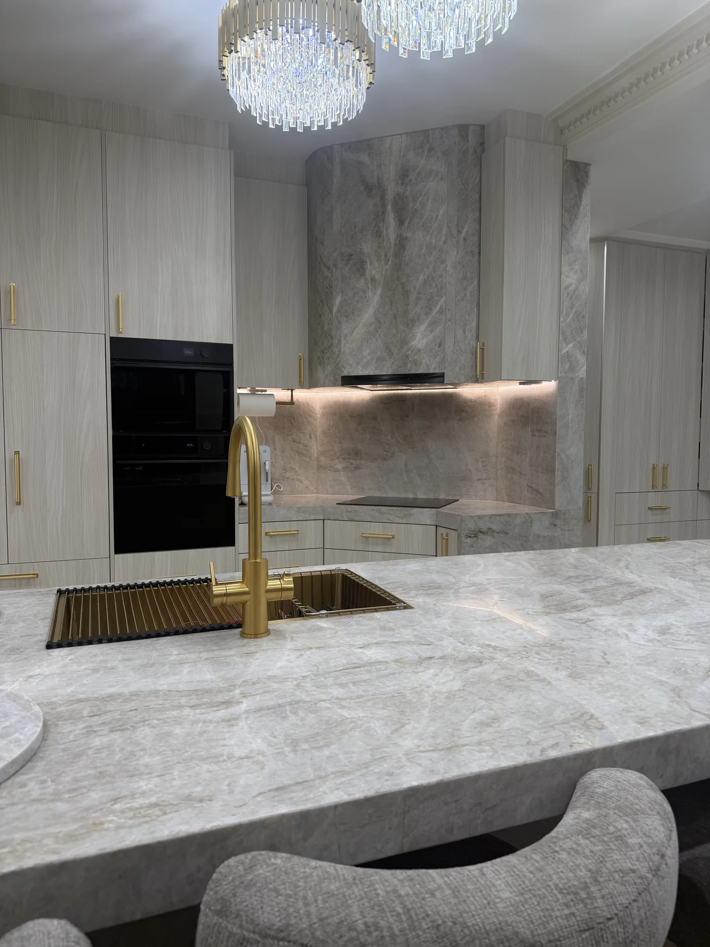 Undermount sink with brass gooseneck mixer, stone-clad rangehood and lit splashback behind