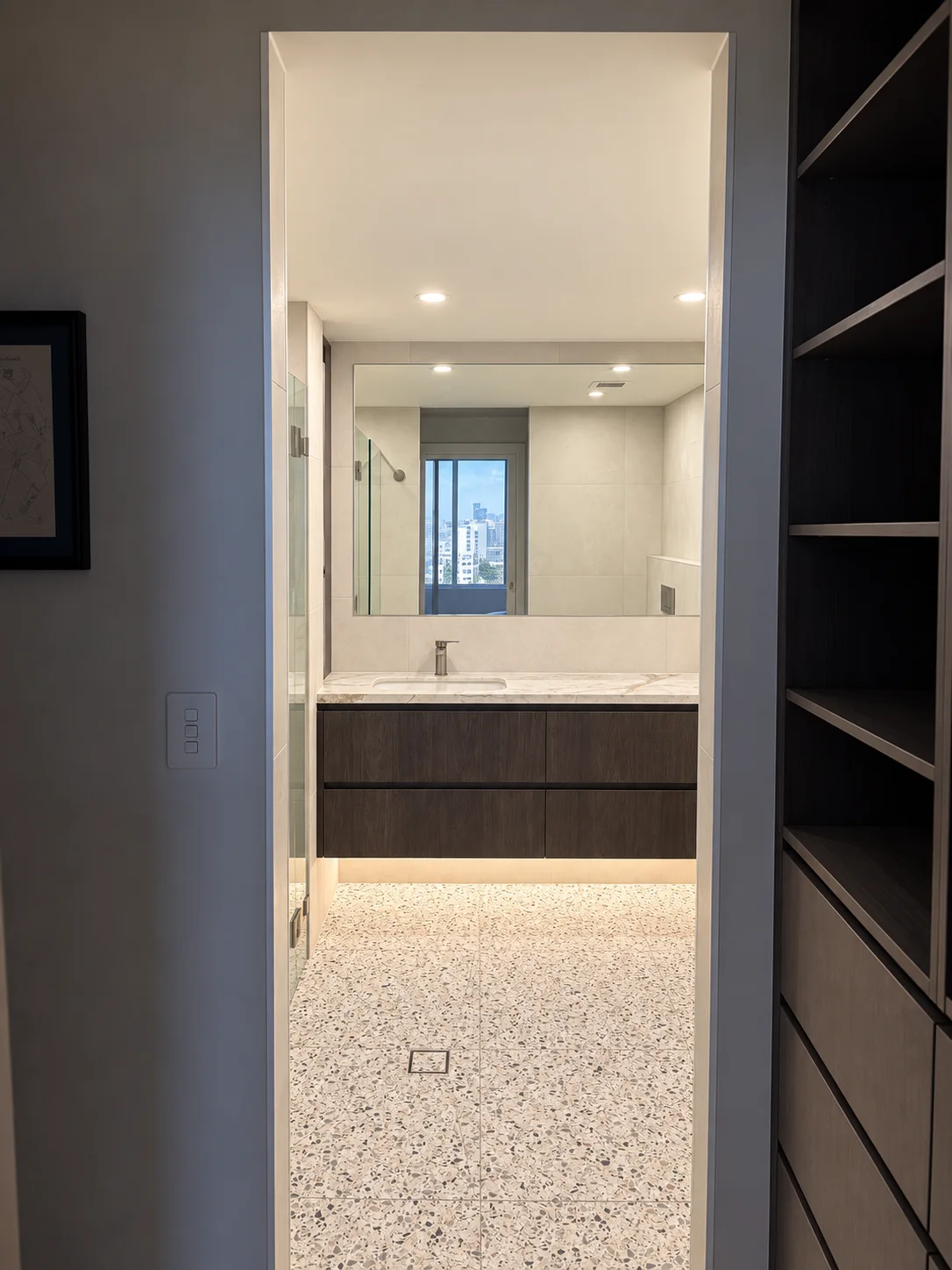 View through a dressing area to a floating timber bathroom vanity and terrazzo-look floor