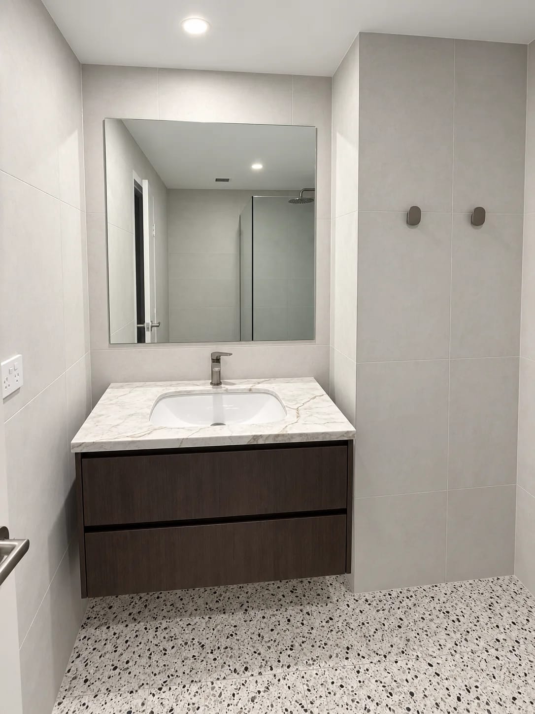 Dark timber floating vanity with veined top, inset basin and large mirror above terrazzo-look tiles