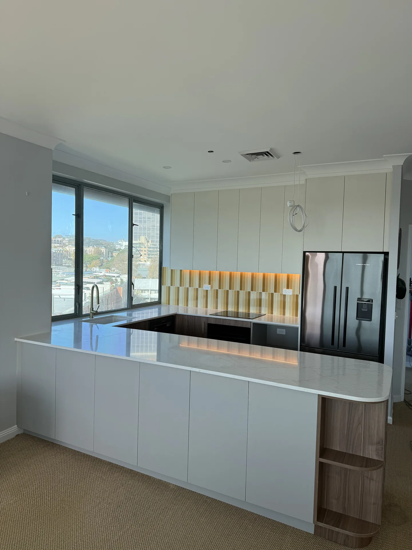 Kitchen peninsula in stone-look benchtop with a lit ochre splashback and bay views beyond