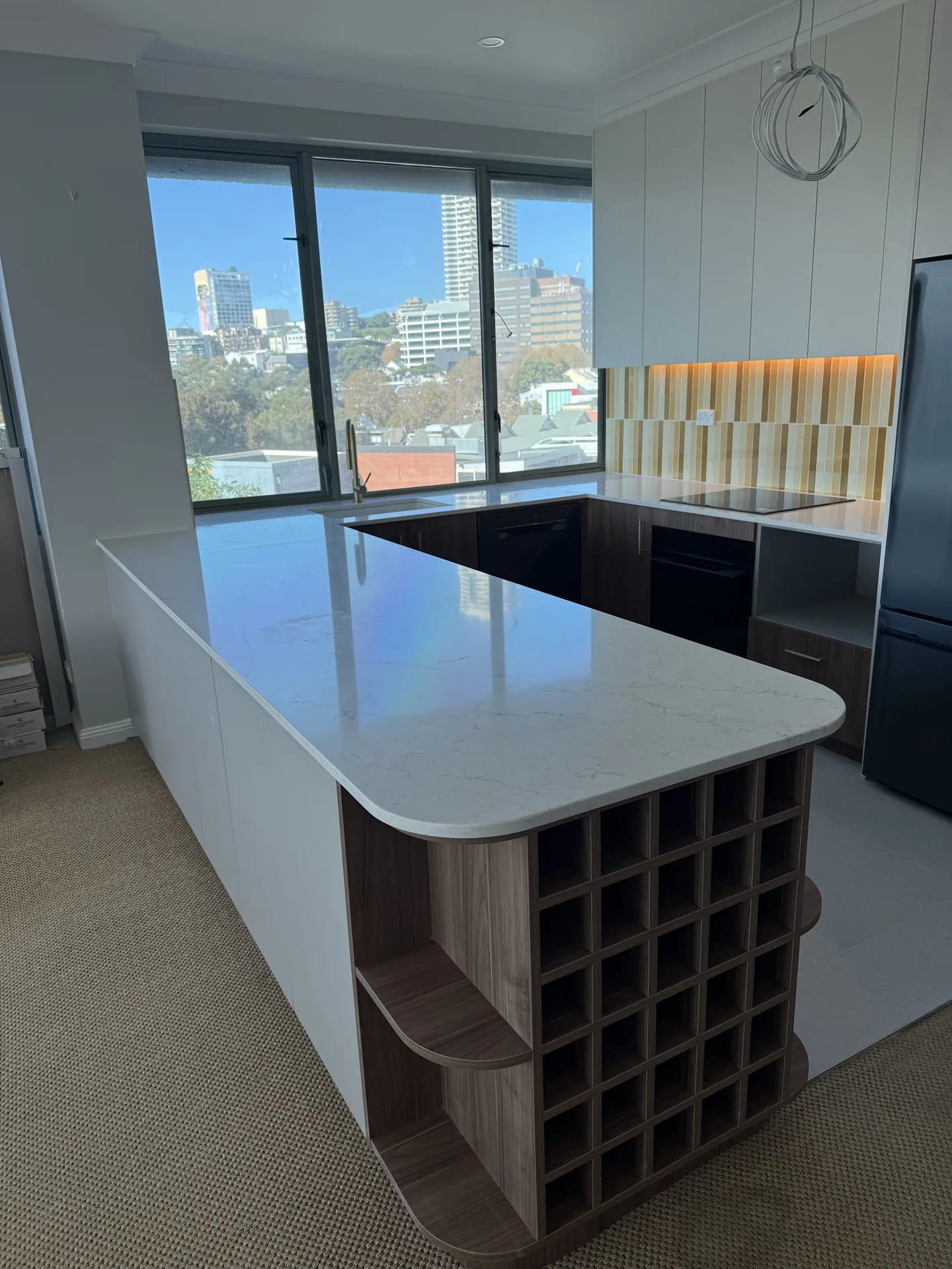Curved stone-look peninsula benchtop above a built-in timber wine rack and open shelves