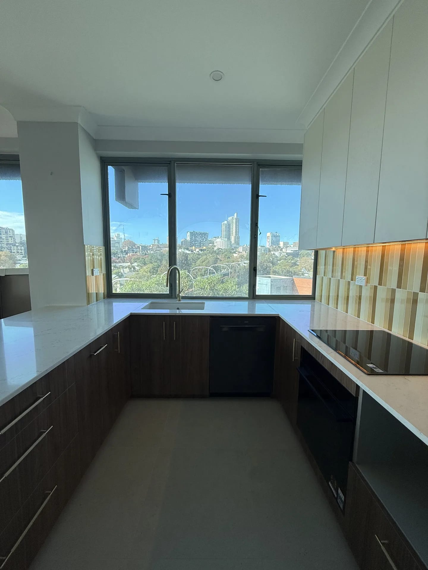 U-shaped kitchen with walnut-look base cabinets, stone benchtops and sink under the window