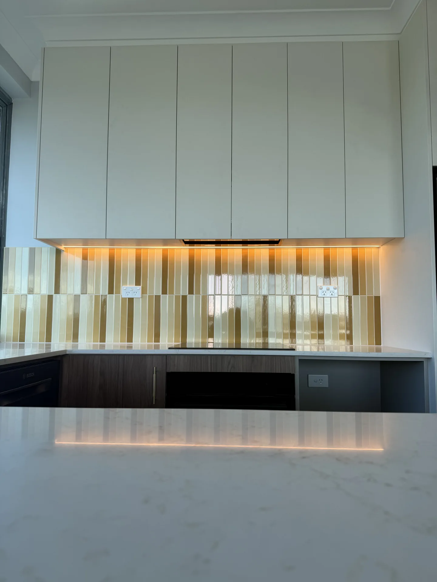 Glazed vertical tile splashback in cream and ochre lit by an LED strip under the cabinets