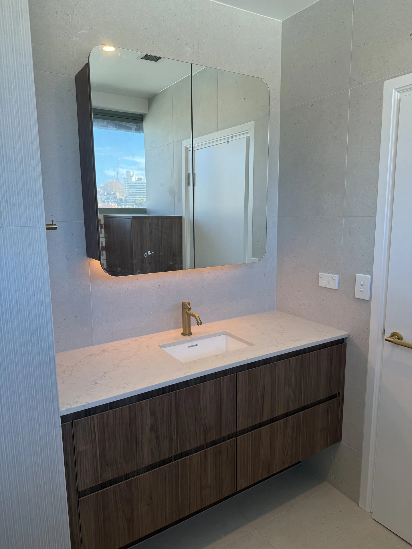 Second bathroom floating vanity below a curved-corner mirror cabinet with backlighting