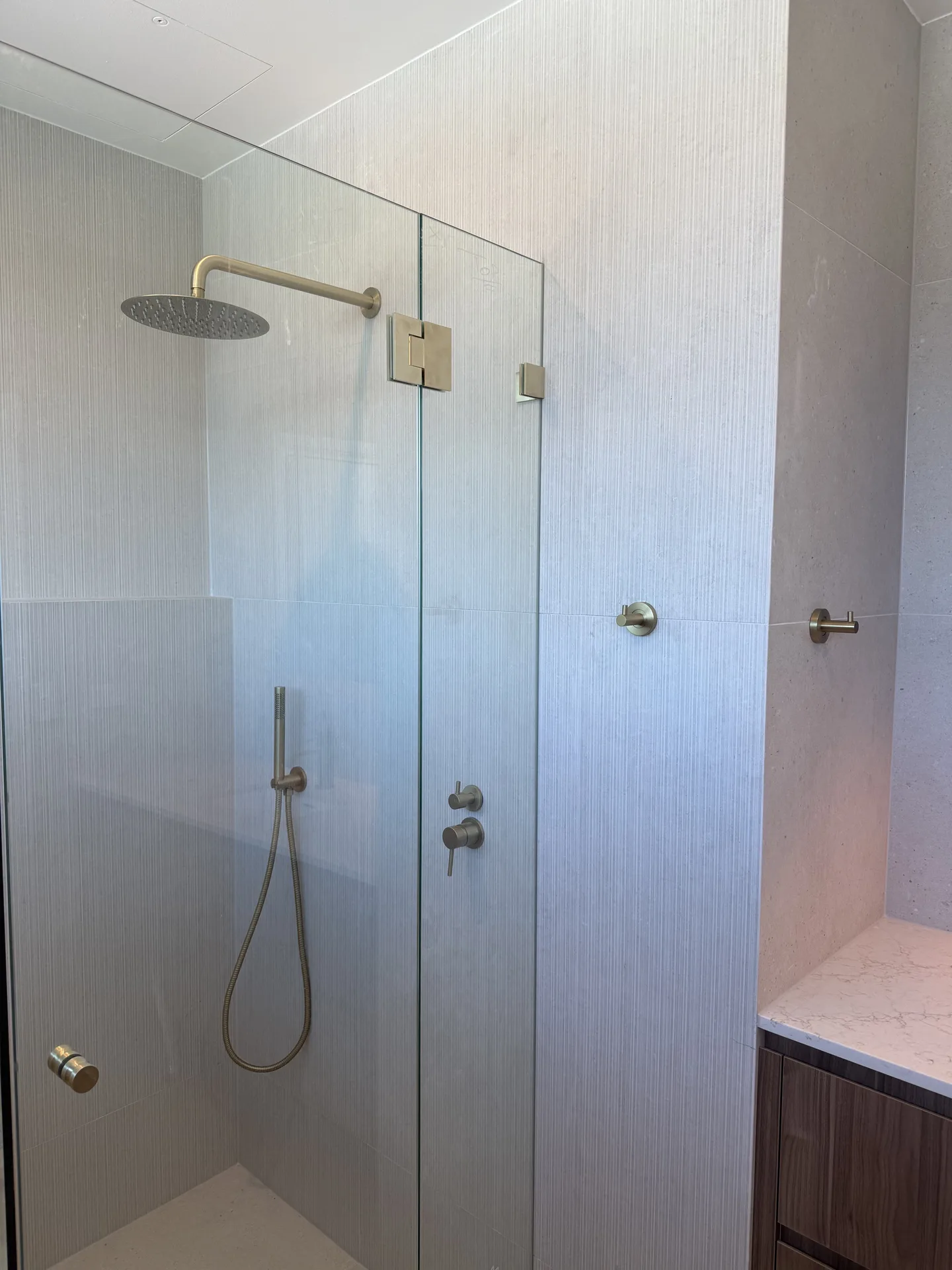 Frameless glass shower with brushed brass tapware against finely fluted pale wall tiles
